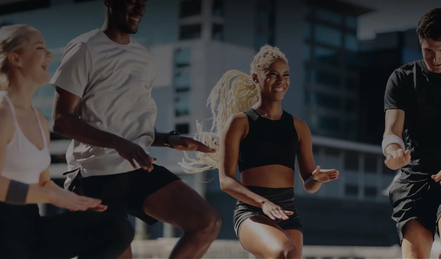 Group of people exercising outdoors in an urban setting, smiling and mid-motion during a group workout.