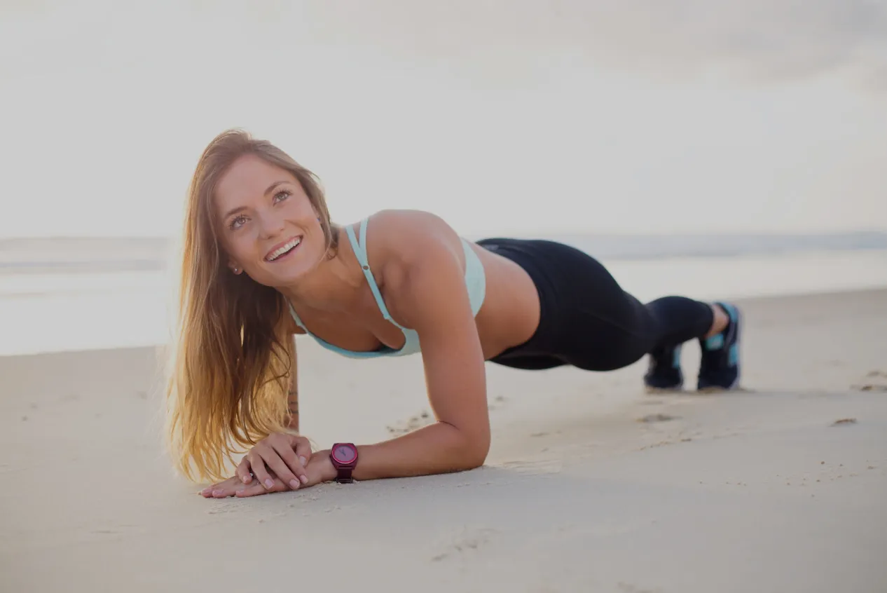 Woman doing a forearm plank on the beach with a big smile.
